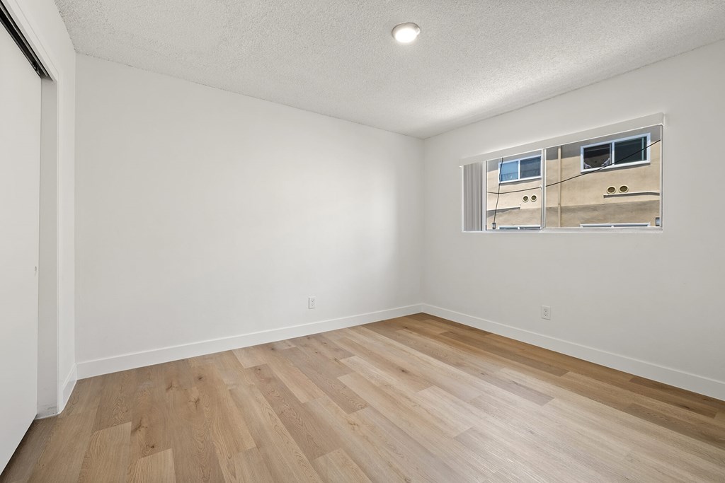 A room with wooden flooring and a window showing a building outside.