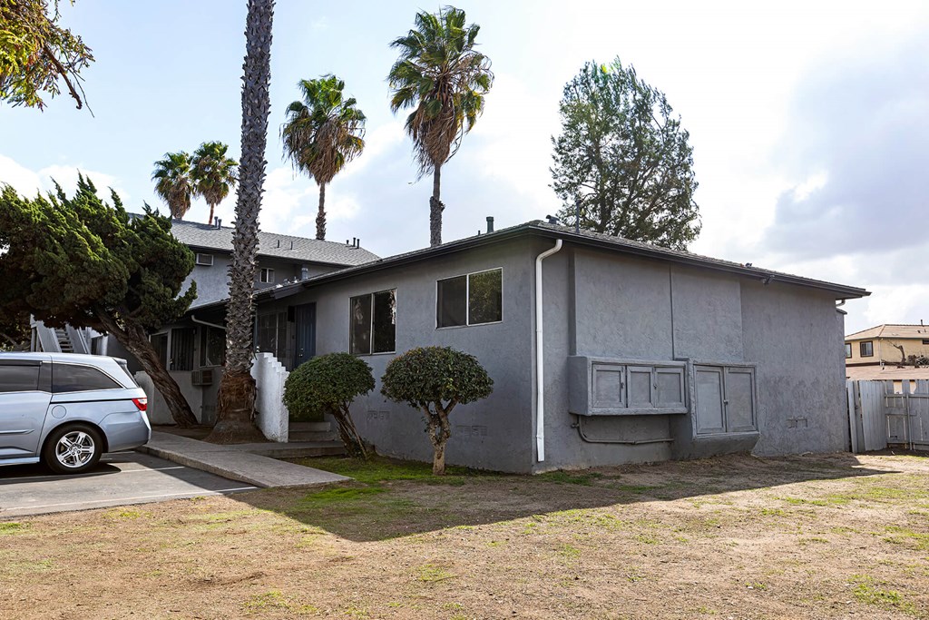 A house with a grey exterior is surrounded by trees and a car is parked in front.