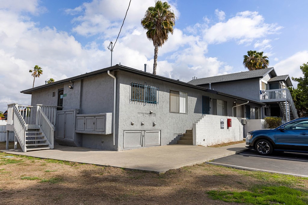 A blue car is parked in front of a house with a palm tree in the background.