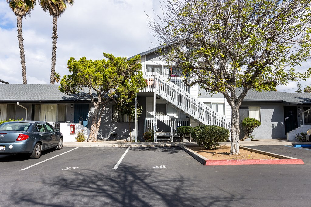 A car is parked in a parking lot in front of a building with a tree.