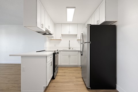 A black refrigerator is in a kitchen with white cabinets.