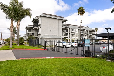 A modern apartment complex with a gated entrance and palm trees.