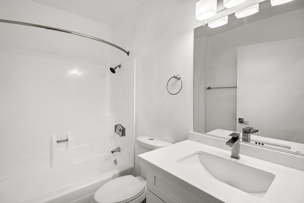 A white bathroom with a toilet, sink, and mirror.
