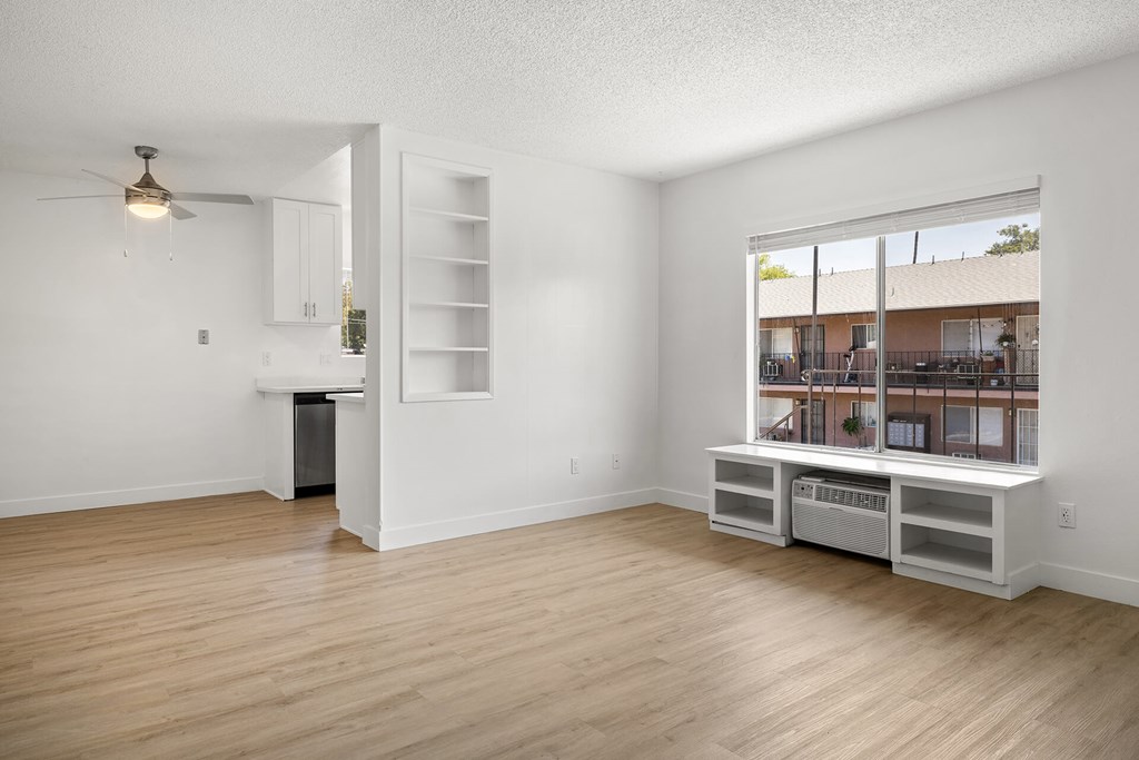 A room with a window overlooking a building and a kitchenette with a sink and a refrigerator.