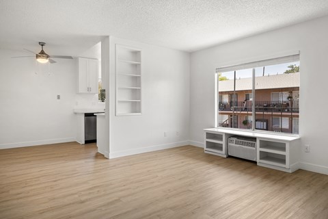 A room with a window overlooking a building and a kitchenette with a sink and a refrigerator.