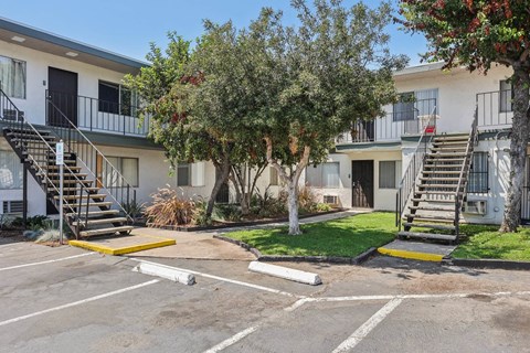 A parking lot with a white building and a tree in the background.