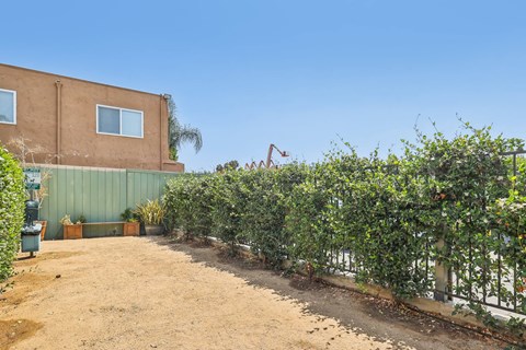 A dirt area with a green fence and a building in the background.