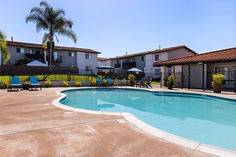 A pool surrounded by a black fence and palm trees.