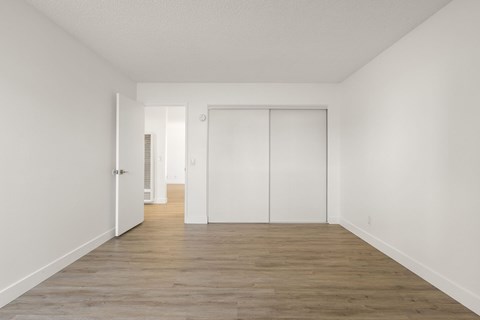 A room with white walls and wooden flooring with a door on the left and a closet on the right.