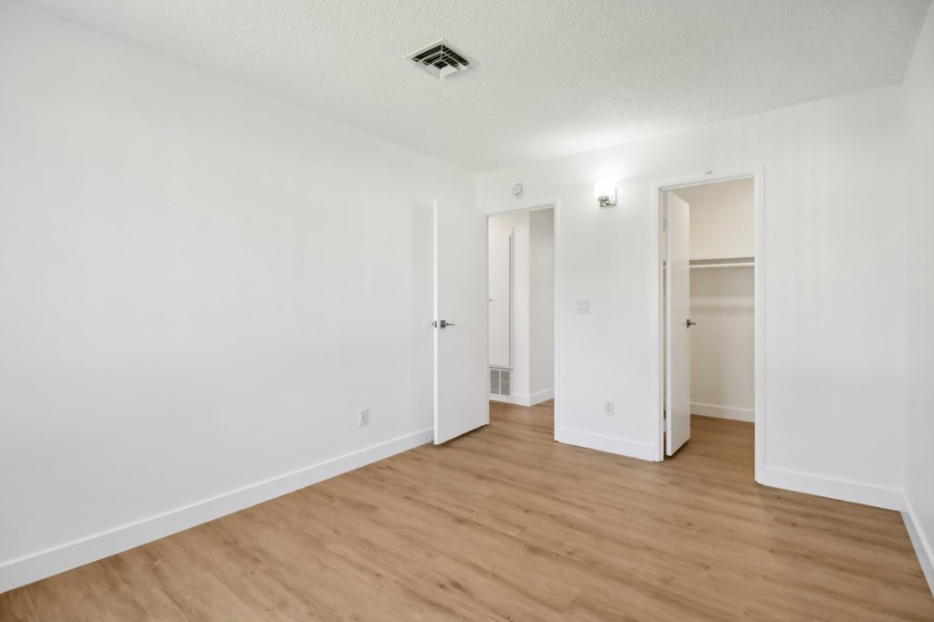 A room with white walls and wooden flooring with two open doors.