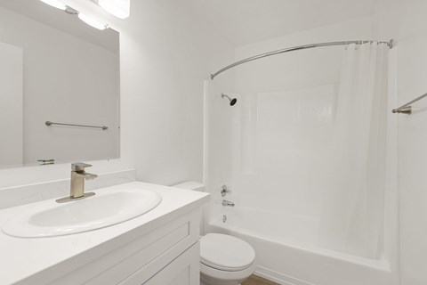 A white bathroom with a sink, toilet, and shower.