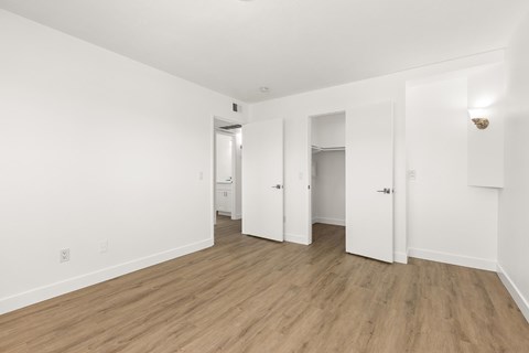 A room with white walls and wooden flooring with a door on the right.