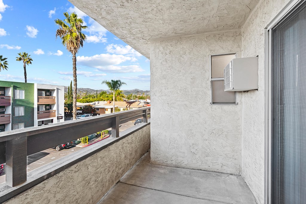 A balcony with a concrete floor and wall with a window and air conditioning unit.