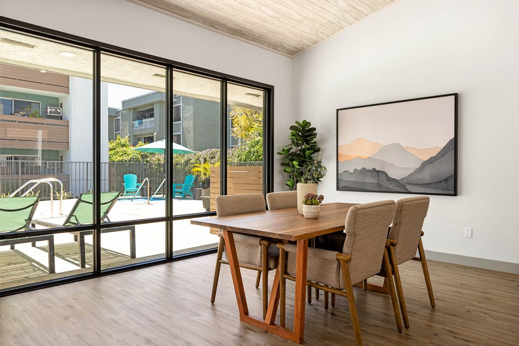A dining room with a wooden table and chairs, a potted plant, and a painting on the wall.