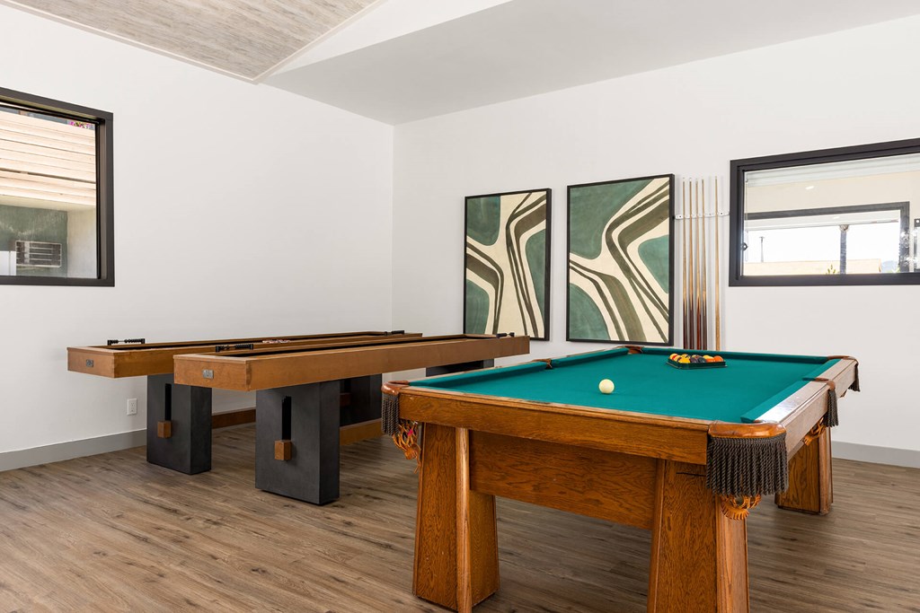 A pool table with a green cloth and a white cue ball is in the foreground of a room with two other pool tables.