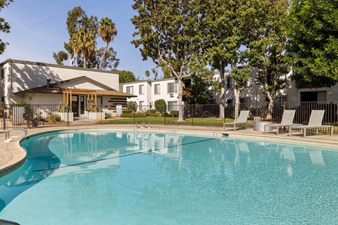 A swimming pool in front of a house with trees in the background.