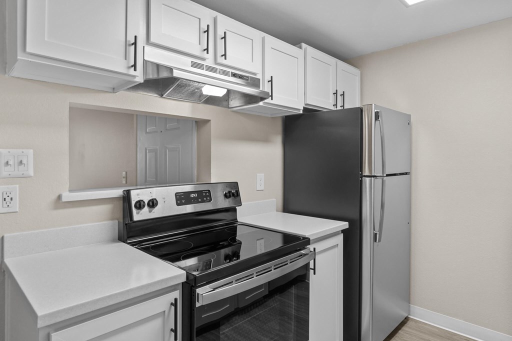A black refrigerator is in a kitchen with white cabinets.