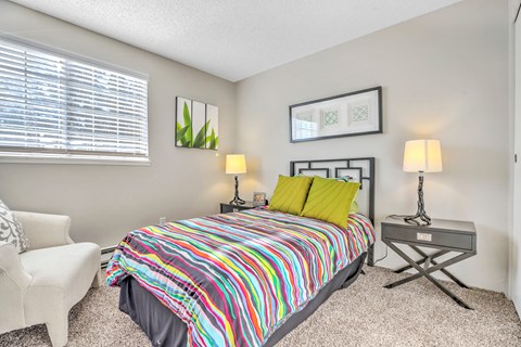 A bedroom with a colorful bedspread and a white chair.