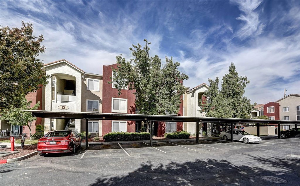 A red car is parked in a parking lot in front of a building.
