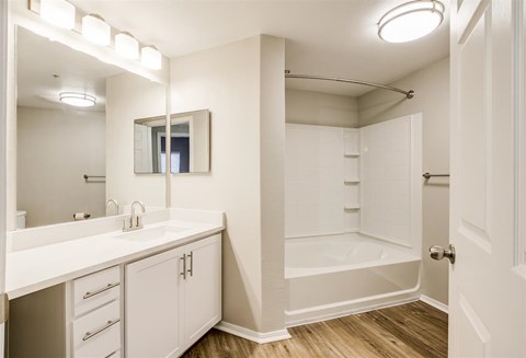 A white bathroom with a vanity, mirror, and shower.