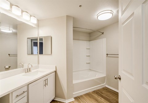 A white bathroom with a large mirror and a bathtub.