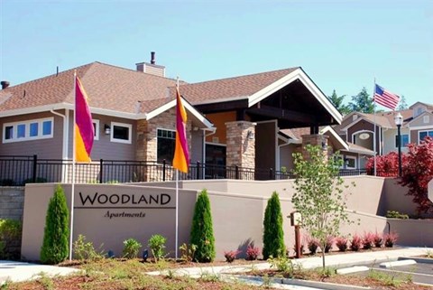 The image shows a building with the name "Woodland Apartments" on a sign in front of it.