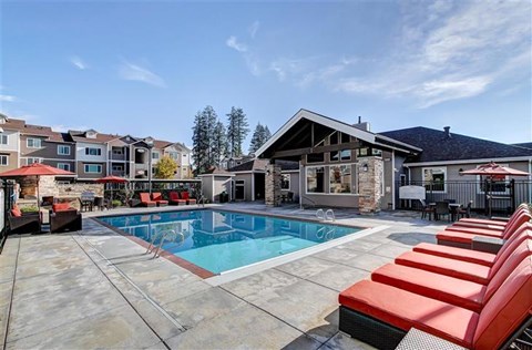 A pool with red chairs and a building in the background.