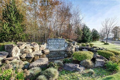 A stone sign for River Trail Apartments sits in front of a grassy area.
