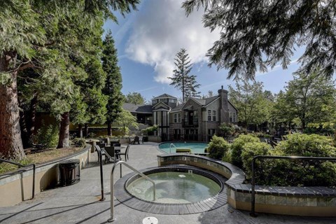 A hot tub sits in the middle of a garden with a house in the background.