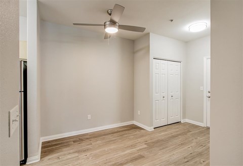 A room with a ceiling fan and light fixture, wooden flooring, and a white door.