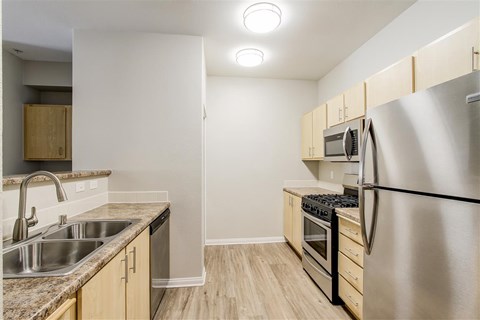 A kitchen with a stainless steel refrigerator, sink, and wooden cabinets.