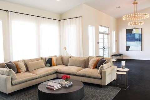 A living room with a large sectional sofa, a coffee table with a book and a flower on it, and a chandelier hanging from the ceiling.
