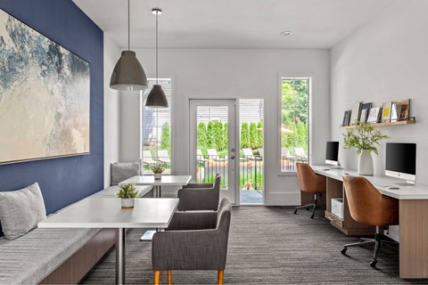 A modern room with a large painting on the wall, a desk with chairs, and a window with blinds.