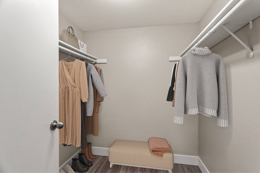 A small closet with a bench and clothes hanging.