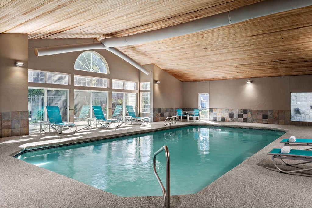 A large indoor swimming pool with a wooden ceiling and a glass wall.