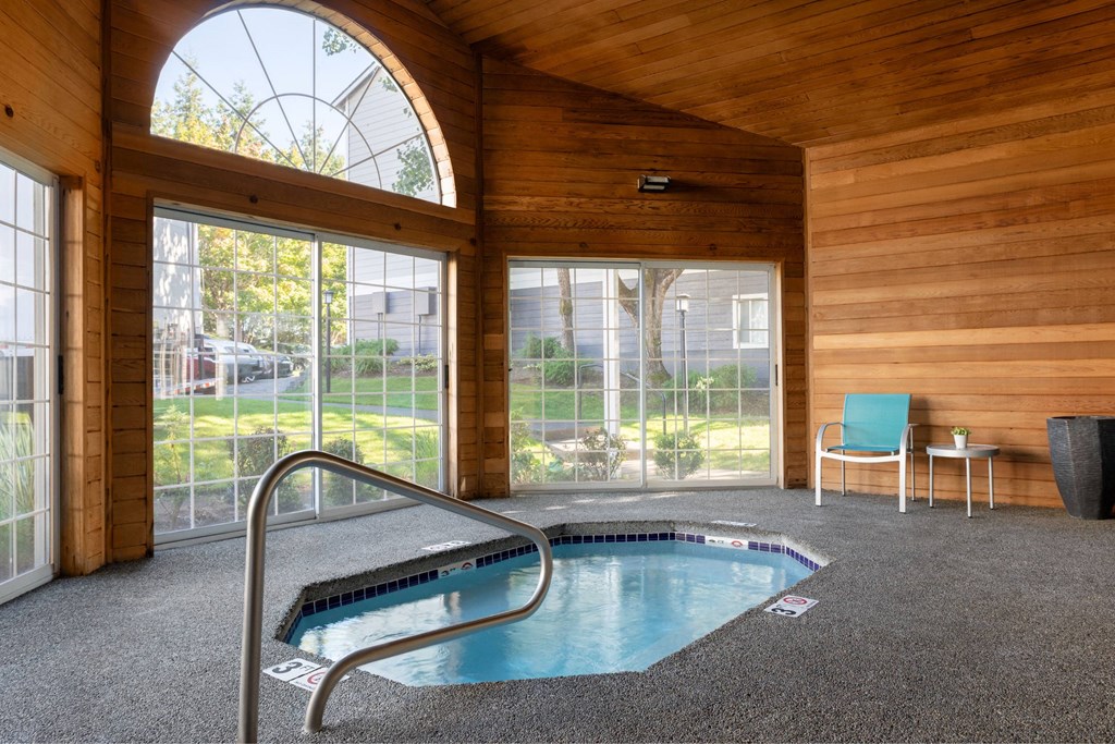 A small indoor swimming pool in a wooden room with a chair and a table.