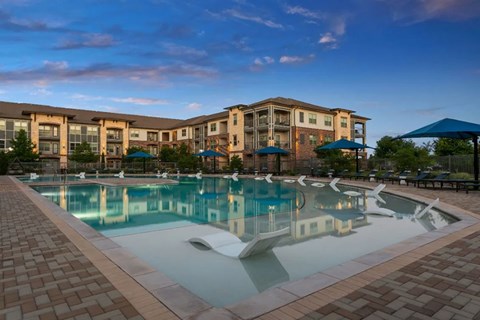 A large swimming pool in front of a building with a sunset sky.