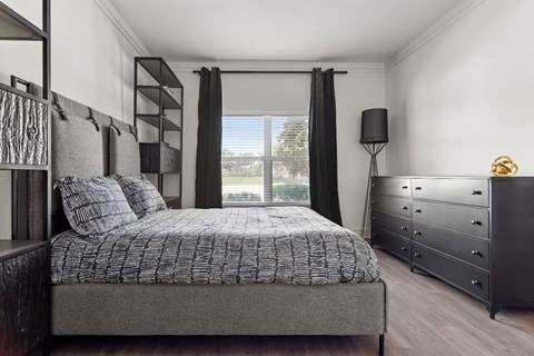 A bedroom with a large bed, a dresser, and a window with black curtains.