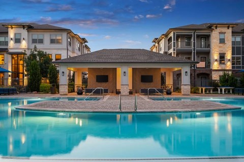 A swimming pool in front of a building with a patio and a barbecue grill.