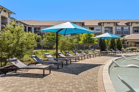 A sunny day at the pool with blue umbrellas and lounge chairs.
