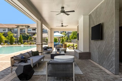 A modern outdoor patio area with a pool, seating, and a ceiling fan.