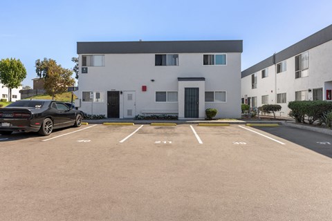 A black car is parked in a parking lot in front of a white building.