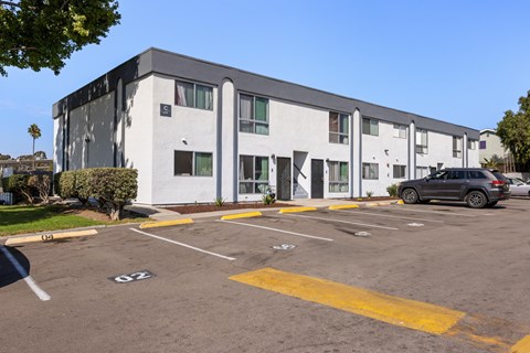 A parking lot in front of a white building with a black car parked in the lot.