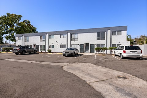A parking lot with a white car and a black car parked in front of a grey building.