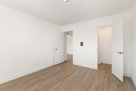 A room with white walls and wood flooring with three doors.