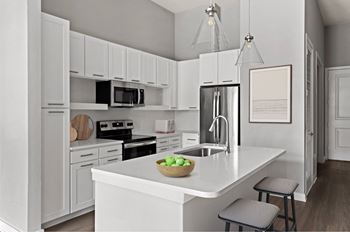 A kitchen with white cabinets and appliances, a bowl of fruit on the island, and a picture frame on the wall.
