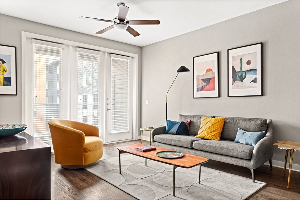 A living room with a grey couch, a yellow chair, a coffee table, and a ceiling fan.