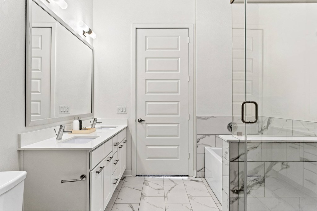 A white bathroom with a marble tub and a white door.