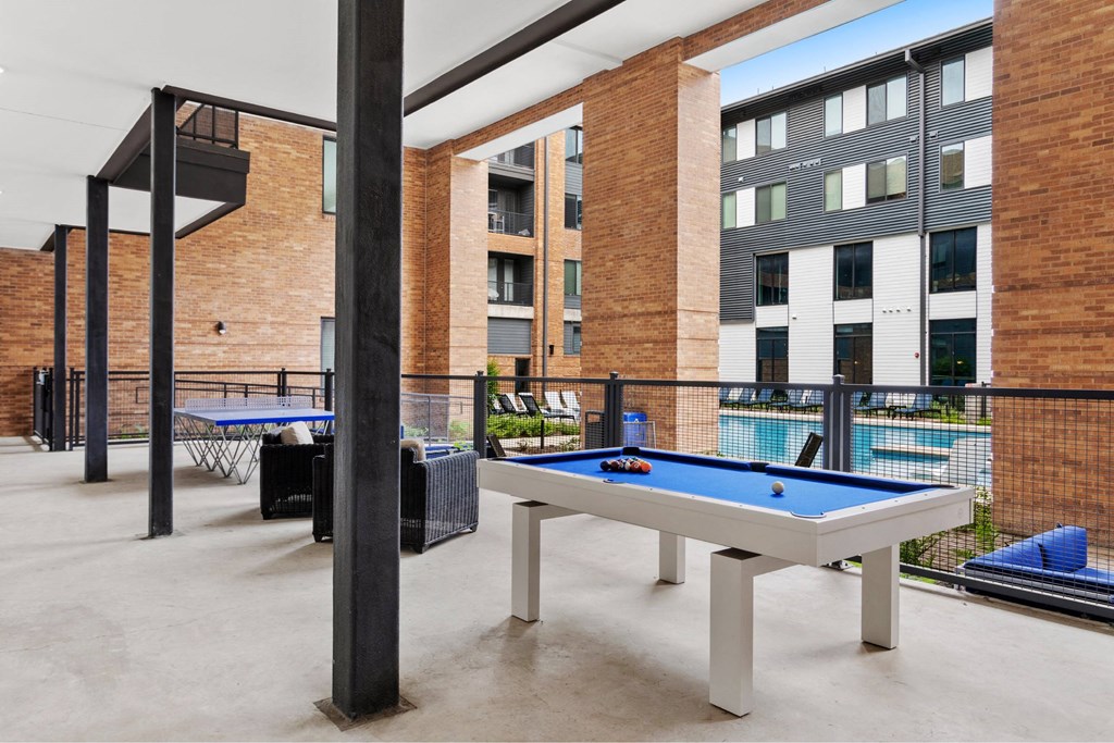 A pool table is surrounded by a black railing in a room with brick walls.
