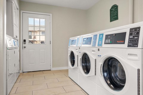 A row of white front load washing machines are lined up in a laundry room.
